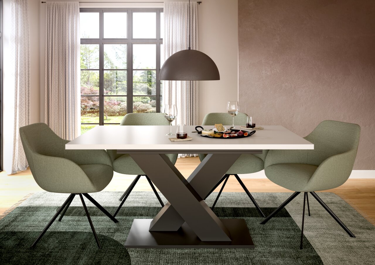 MID.YOU Esstisch MOTION Moderner Esstisch mit X-förmigem Gestell und vier grünen Stühlen in einem hellen Raum mit großem Fenster, seitliche Perspektive.