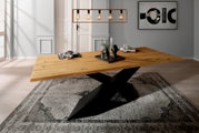 Moderner Esstisch aus Holz mit schwarzem Kreuzfußgestell, seitliche Perspektive, dekoriert mit Geschirr und Kerzen auf einem Teppich.