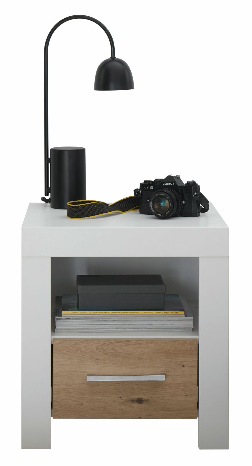 Nachtkommode in moderner Perspektive mit weißer Oberfläche, schwarzer Lampe, Kamera und Büchern, sowie einer Schublade in Holzoptik.