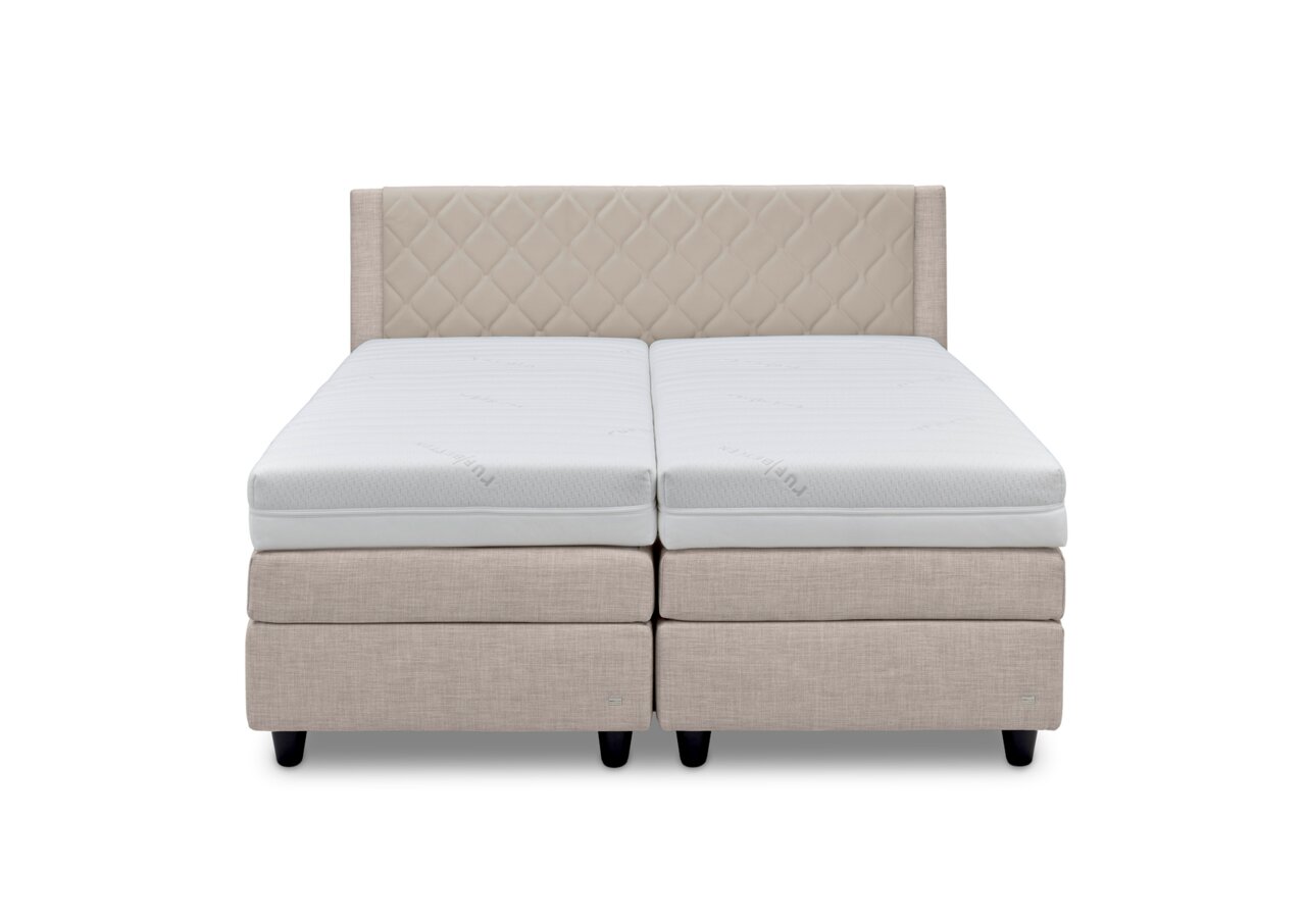 Vooraanzicht van een elegant boxspringbed met een beige, doorgestikt hoofdeinde en witte matrassen.