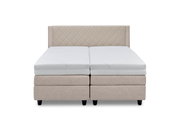 Vooraanzicht van een elegant boxspringbed met een beige, doorgestikt hoofdeinde en witte matrassen.