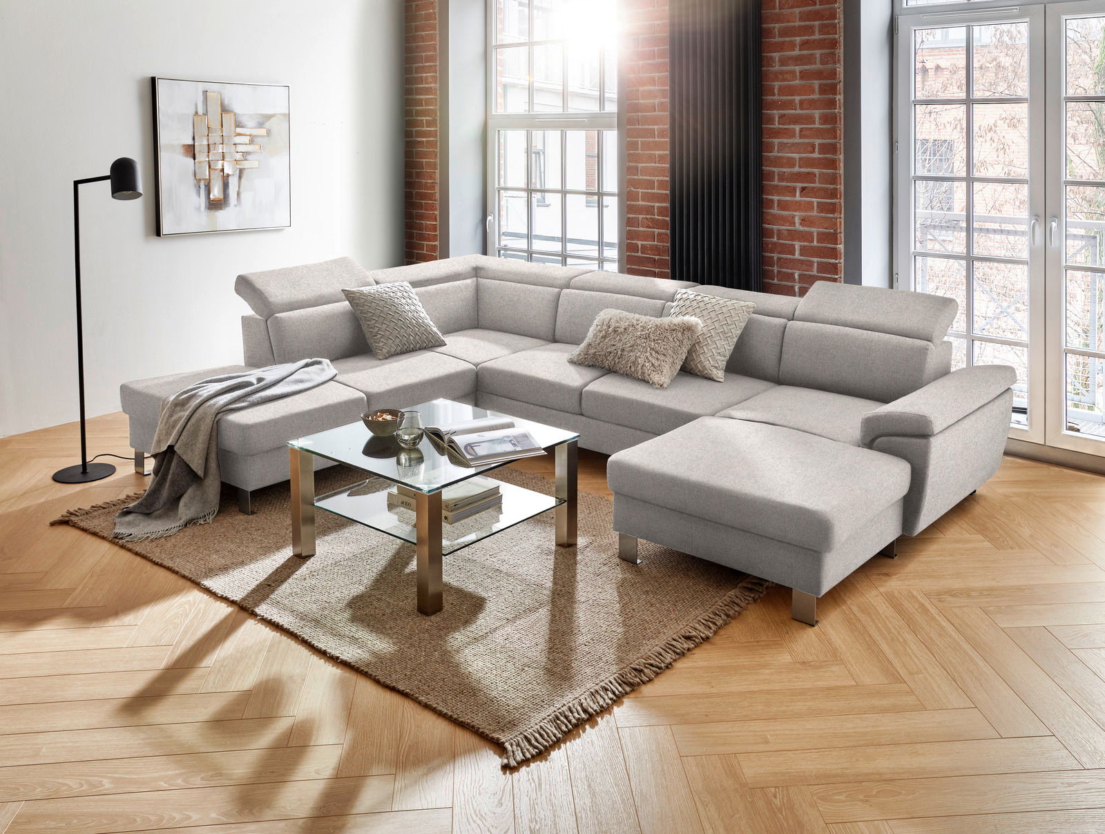 Moderne graue Rundecke in U-Form in einem hellen Wohnzimmer mit großen Fenstern, Holzboden und stilvoller Dekoration, Perspektive von vorne links.