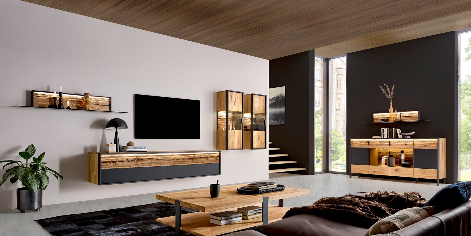 Modernes Wohnzimmer mit Holz- und Anthrazit-Möbeln, schwebendem TV-Lowboard, Wandregal und Vitrinen mit LED-Beleuchtung sowie Sideboard; Perspektive: Weitwinkel-Ansicht schräg von vorne.