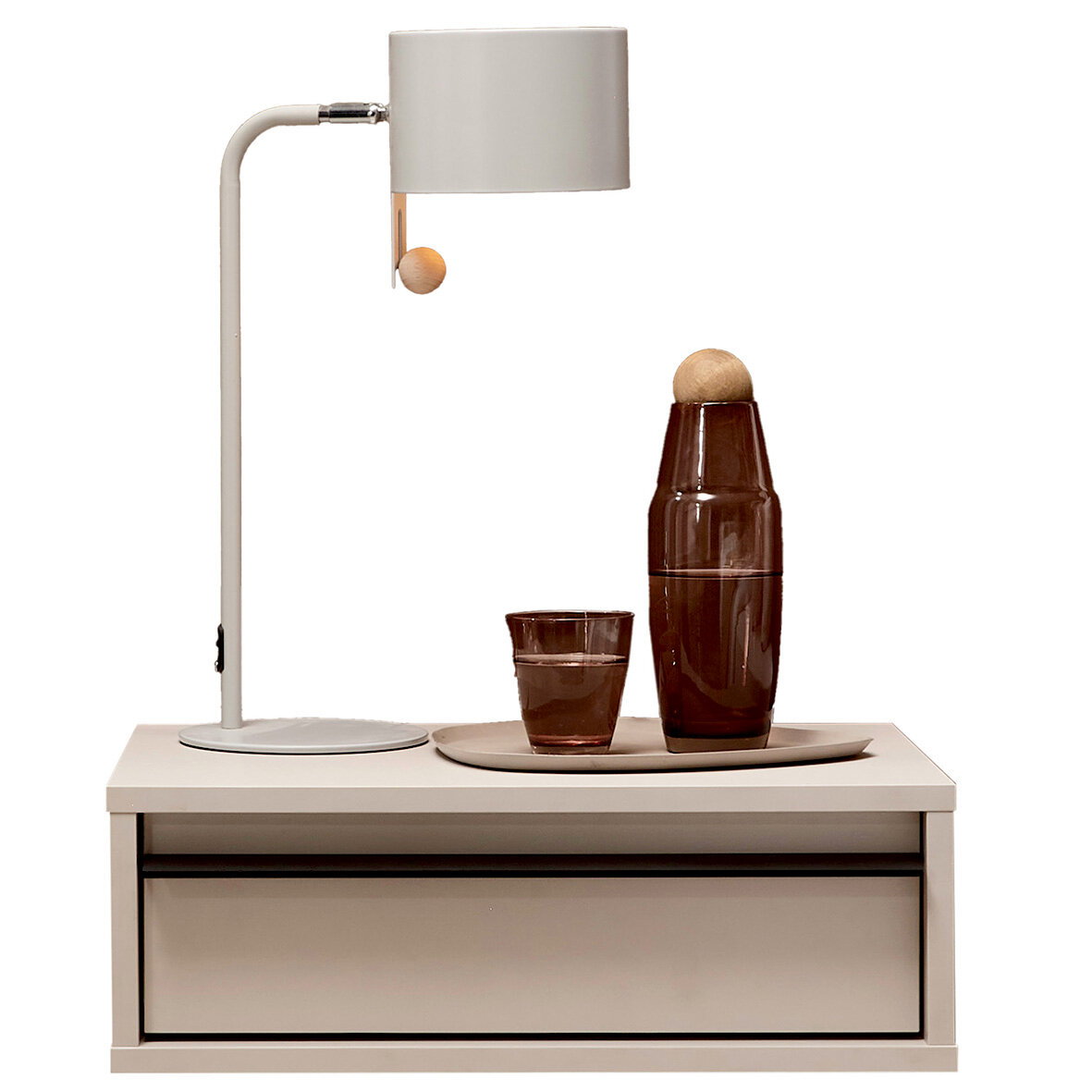 Frontansicht: moderne weiße Tischlampe mit zylindrischem Schirm und Holz-Zugschalter auf einem weißen Nachttisch; daneben braune Glasflasche und Glas auf Tablett