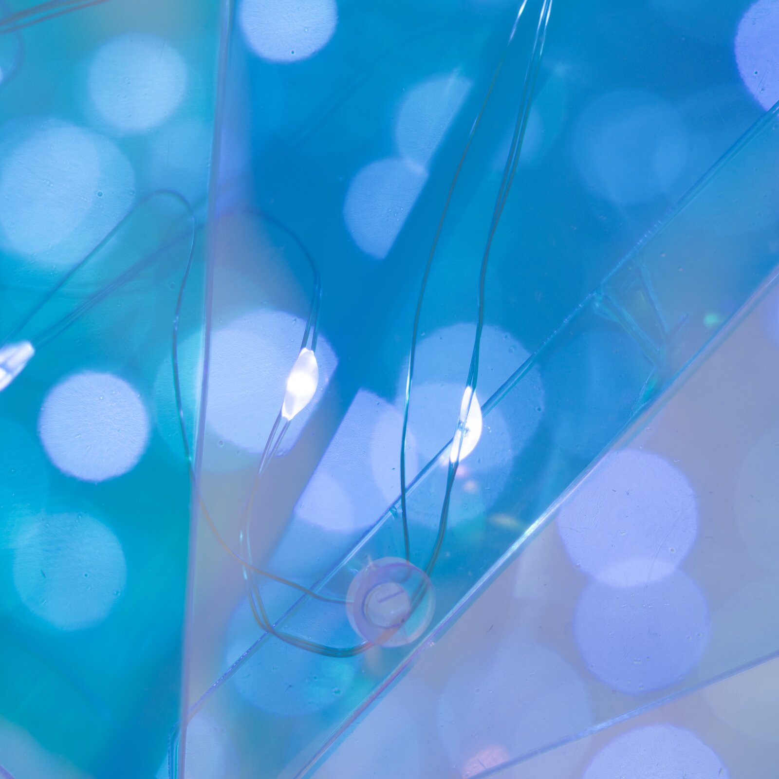 Abstrakte Nahaufnahme aus leicht schräger Draufsicht: transparente, blau schimmernde Kunststofffolien mit weichen, runden Lichtreflexen und feinen Linien.