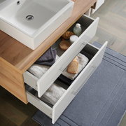 Badezimmerkombination mit Waschbecken und zwei geöffneten Schubladen, gefüllt mit Handtüchern und Pflegeprodukten, aus der Vogelperspektive.