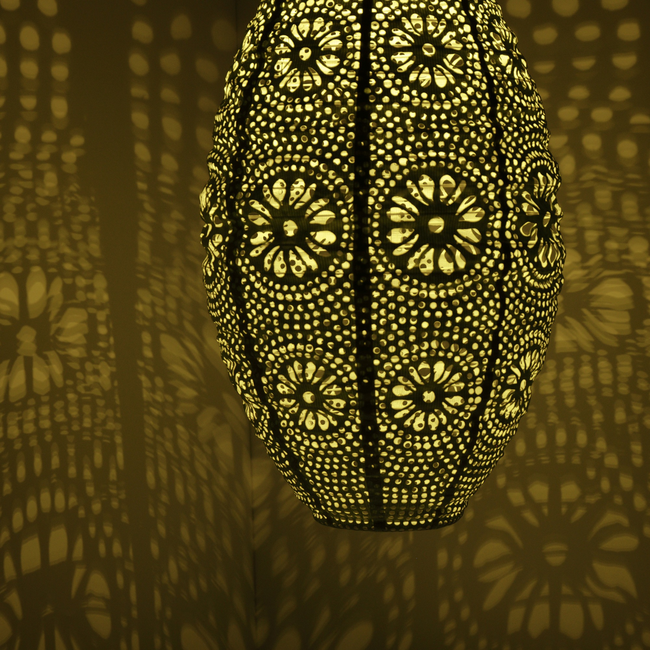 Nahaufnahme einer dekorativen Solar Laterne mit filigranem Muster, das ein warmes Licht und faszinierende Schatten an die Wand wirft.