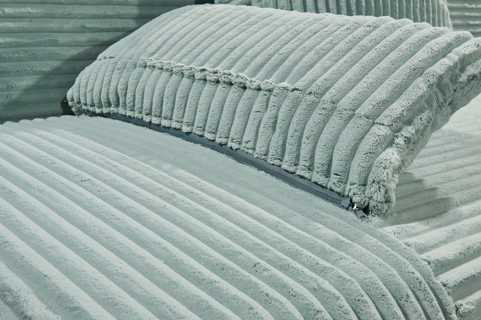 Nahaufnahme eines Funktionssofas mit weichem, geripptem Stoffbezug in hellem Grün, seitliche Perspektive.