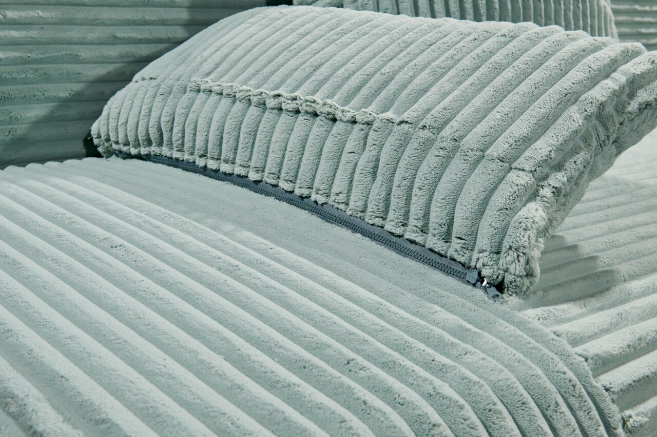 Nahaufnahme eines Funktionssofas mit weichem, geripptem Stoffbezug in hellem Grün, seitliche Perspektive.