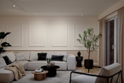 Modernes Wohnzimmer mit hellem L-förmigem Sofa, schwarzen und beigen Kissen, runden Couchtischen aus Holz und Schwarz sowie großer Zimmerpflanze neben Fenster; Perspektive: frontale Weitwinkelaufnahme auf Sitzbereich und Wandpaneele.