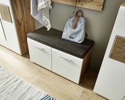 Garderoben-Set mit weißem Schrank und Holzdetails, grauem Sitzpolster und Rucksack, aus seitlicher Perspektive fotografiert.