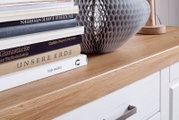 Van voren schuin gefotografeerd: houten oppervlak van een ladekast met een stapel boeken en een grote grijze decoratieve schaal met structuur
