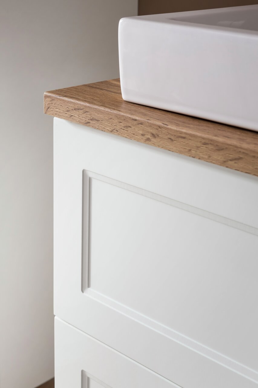 Close-up van een wastafelcombinatie met een witte wastafel en een houten werkblad, gezien vanaf de zijkant
