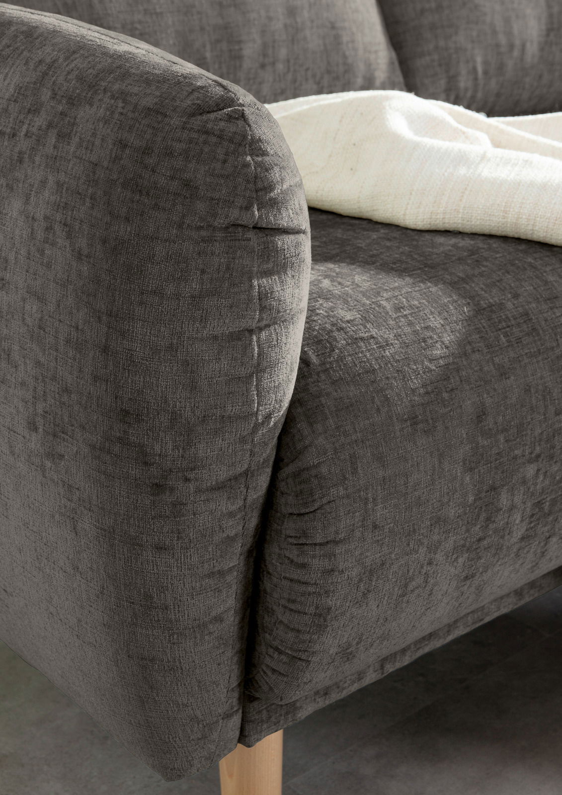 Nahaufnahme einer grauen Sofaecke mit Holzbeinen und einer weißen Decke, von der Seite betrachtet.