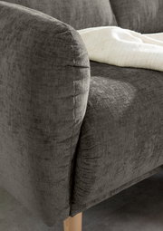 Nahaufnahme einer grauen Sofaecke mit Holzbeinen und einer weißen Decke, von der Seite betrachtet.