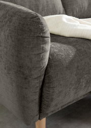 Nahaufnahme einer grauen Sofaecke mit Holzbeinen und einer weißen Decke, von der Seite betrachtet.