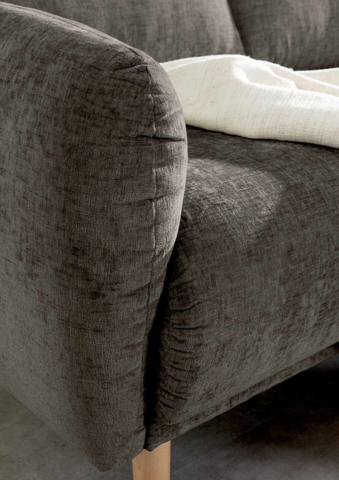 Nahaufnahme einer grauen Sofaecke mit Holzbeinen und einer weißen Decke, von der Seite betrachtet.