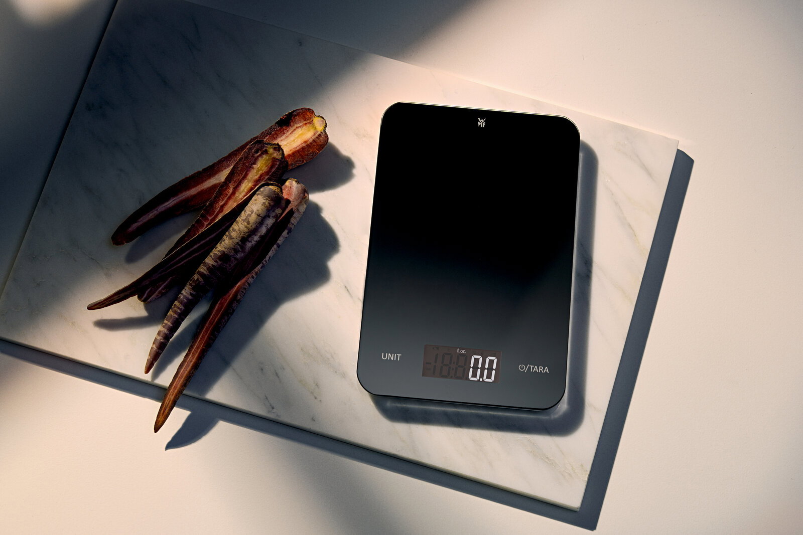 WMF Digitale Küchenwaage 23x15cm Digitale Küchenwaage in Schwarz, von oben fotografiert, neben lila Karotten auf einer Marmorplatte.