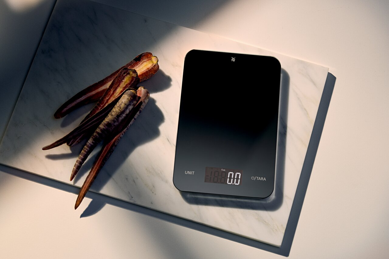 WMF Digitale Küchenwaage 23x15cm Digitale Küchenwaage in Schwarz, von oben fotografiert, neben lila Karotten auf einer Marmorplatte.