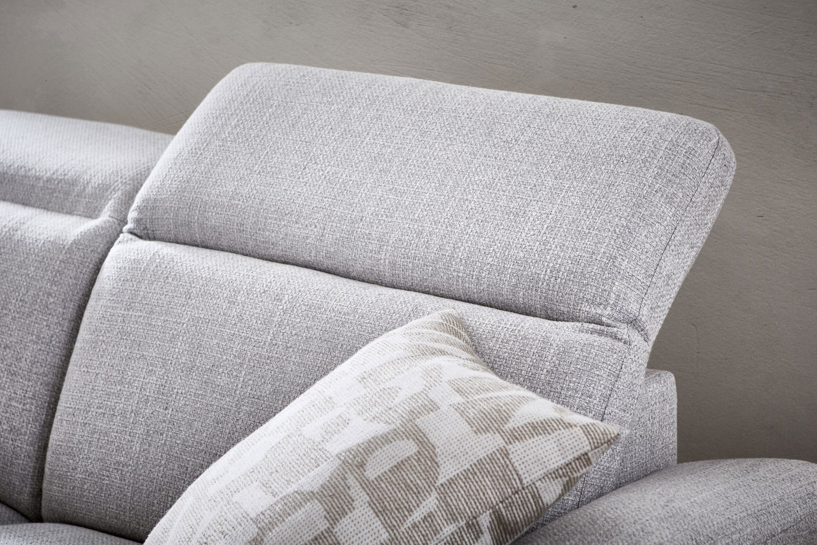 Nahaufnahme eines grauen Longchairs mit verstellbarer Kopfstütze und dekorativem Kissen, seitliche Perspektive.