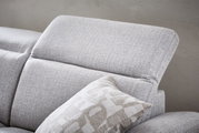 Nahaufnahme eines grauen Longchairs mit verstellbarer Kopfstütze und dekorativem Kissen, seitliche Perspektive.