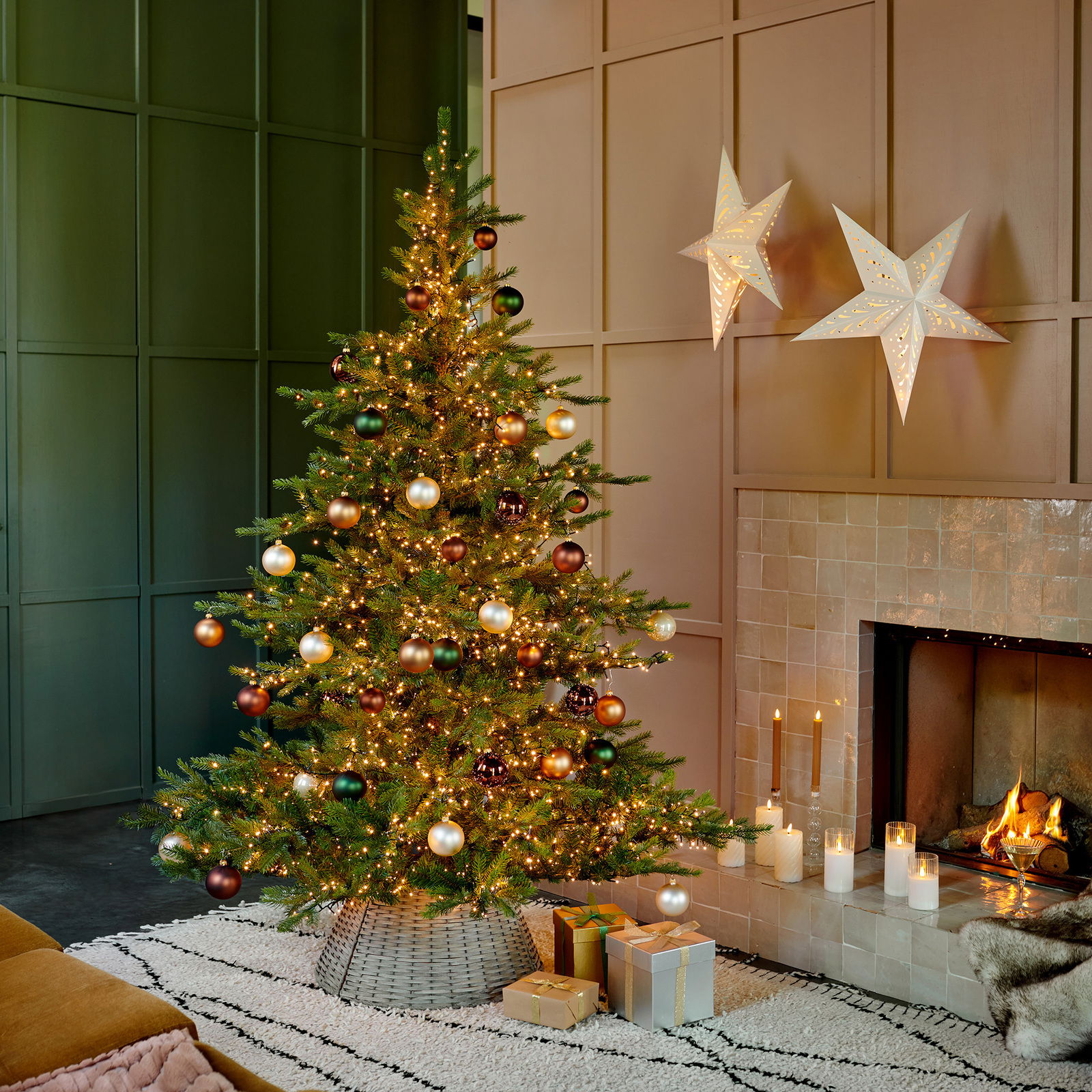 Weihnachtsbaum mit Kugeln und Lichtern, seitliche Perspektive, neben einem Kamin mit brennenden Kerzen und Geschenken.