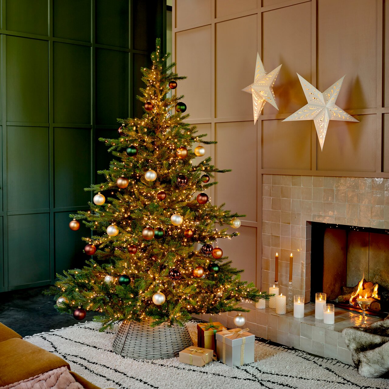 Weihnachtsbaum mit Kugeln und Lichtern, seitliche Perspektive, neben einem Kamin mit brennenden Kerzen und Geschenken.