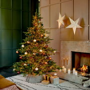 Weihnachtsbaum mit Kugeln und Lichtern, seitliche Perspektive, neben einem Kamin mit brennenden Kerzen und Geschenken.