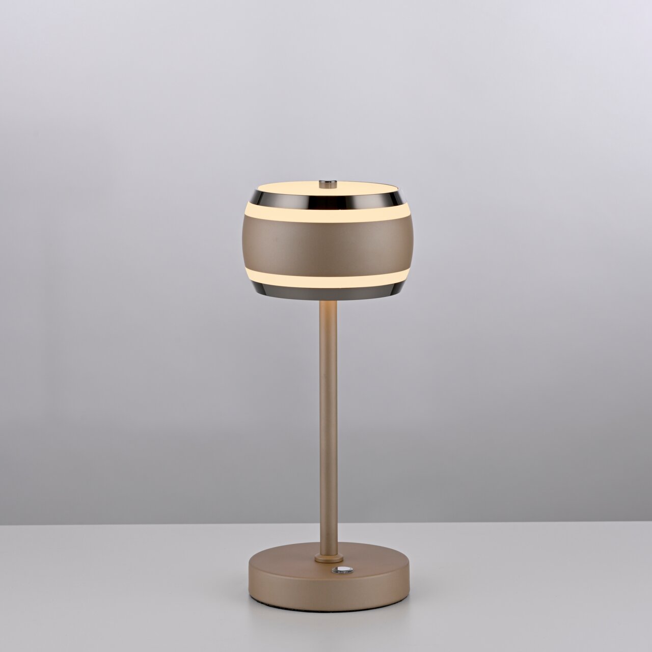 Moderne Akku-Tischleuchte in seitlicher Perspektive mit rundem, zweifarbigem Lampenschirm und schlankem Standfuß auf einem Tisch.