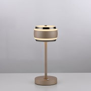 Moderne Akku-Tischleuchte in seitlicher Perspektive mit rundem, zweifarbigem Lampenschirm und schlankem Standfuß auf einem Tisch.