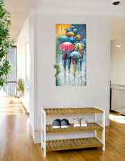 Modernes Wandbild/Leinwand im Hochformat mit bunten Regenschirmen und Personen im Regen, frontal aus Augenhöhe an einer weißen Flurwand über einer Holz-Schuhbank aufgenommen.