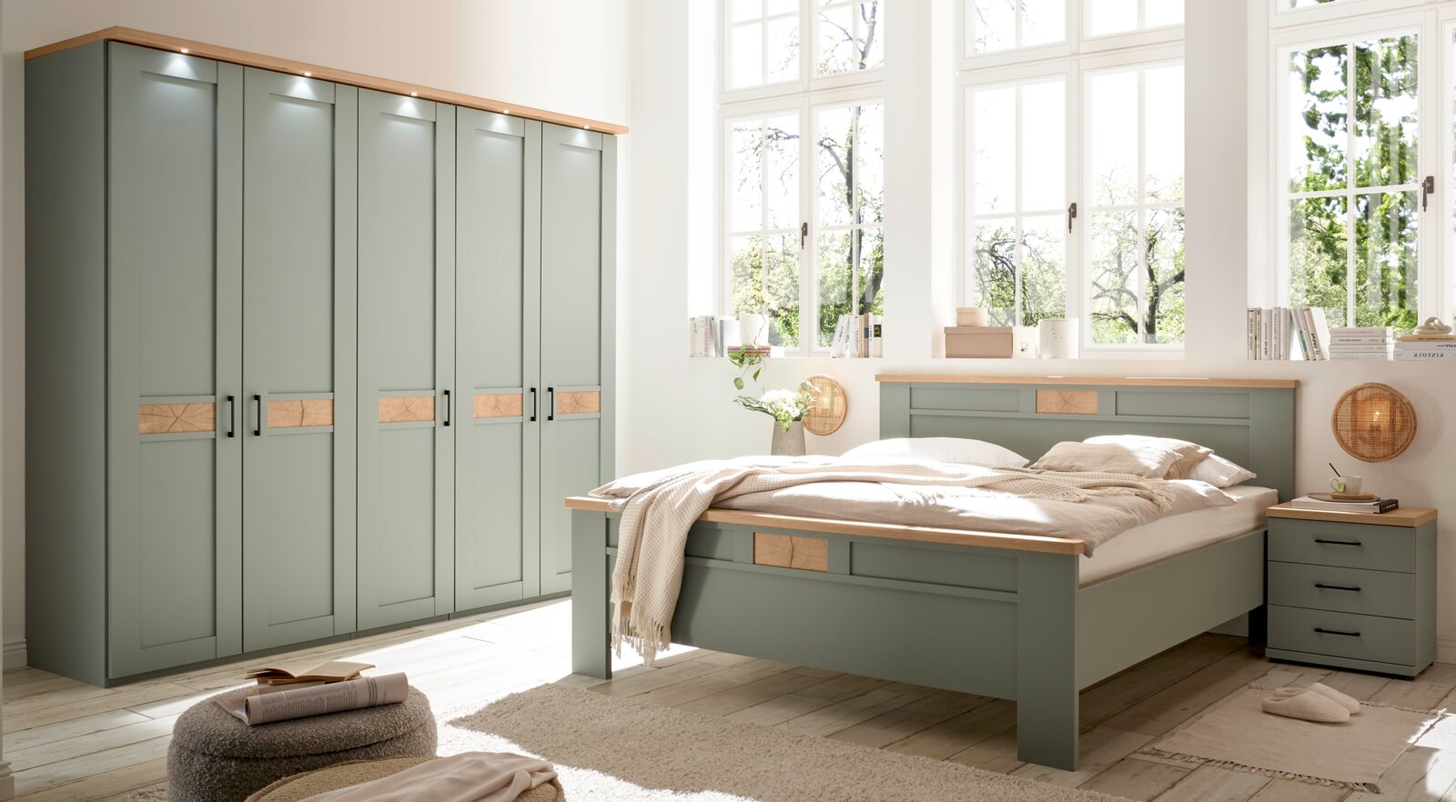 Helles Schlafzimmer-Set mit großem Bett, Nachttisch und mehrtürigem Kleiderschrank in Salbeigrün mit Holzdetails, fotografiert in schräger Frontansicht aus leicht erhöhter Perspektive.