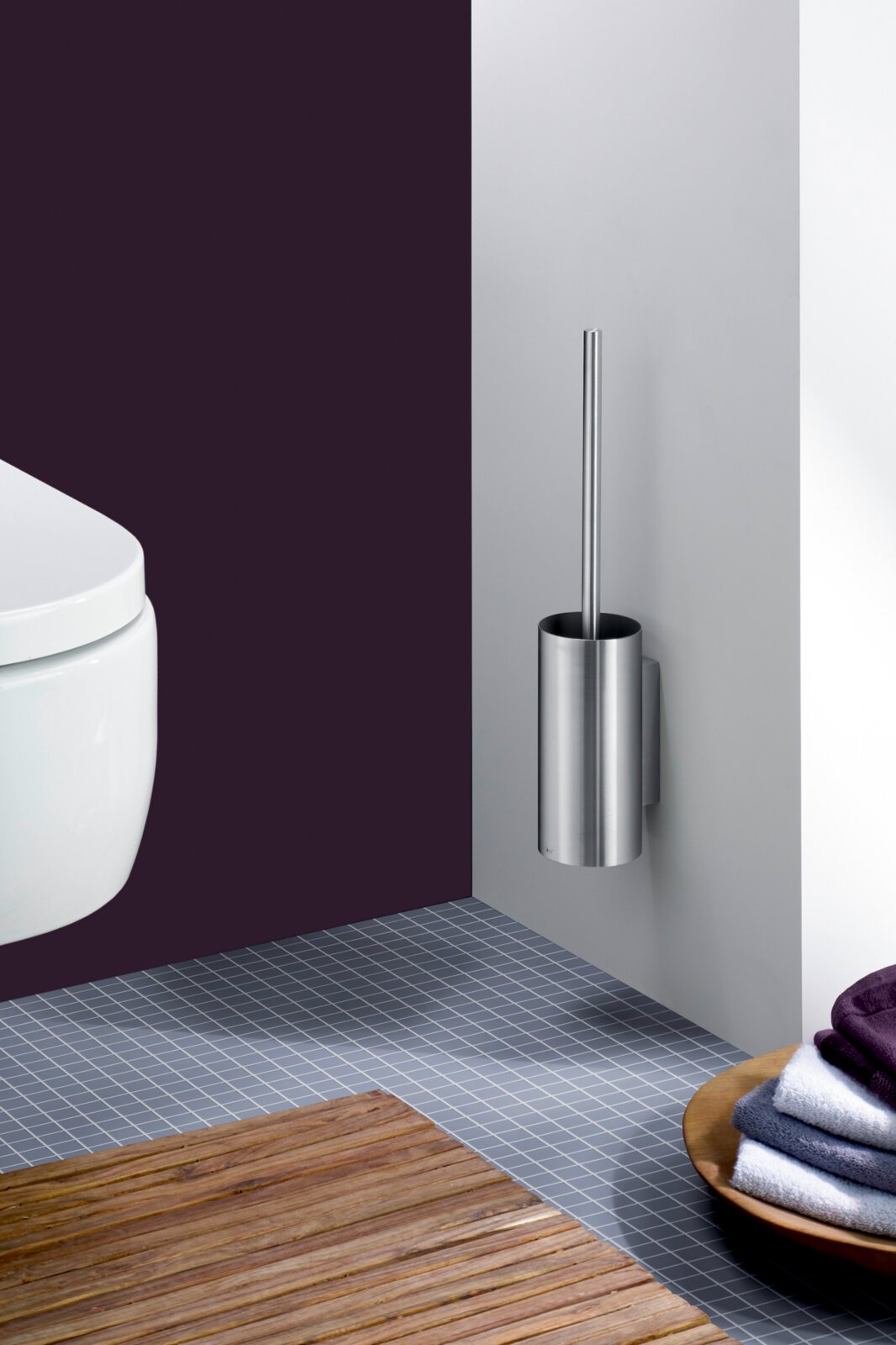 Wandmontierte WC-Bürstengarnitur aus gebürstetem Edelstahl mit zylindrischem Behälter und Griff, seitliche Frontansicht im Badezimmer neben einem weißen WC