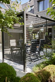 Moderner Sichtschutz aus Aluminium auf einer Terrasse, seitliche Perspektive, umgeben von Pflanzen und Gartenmöbeln.