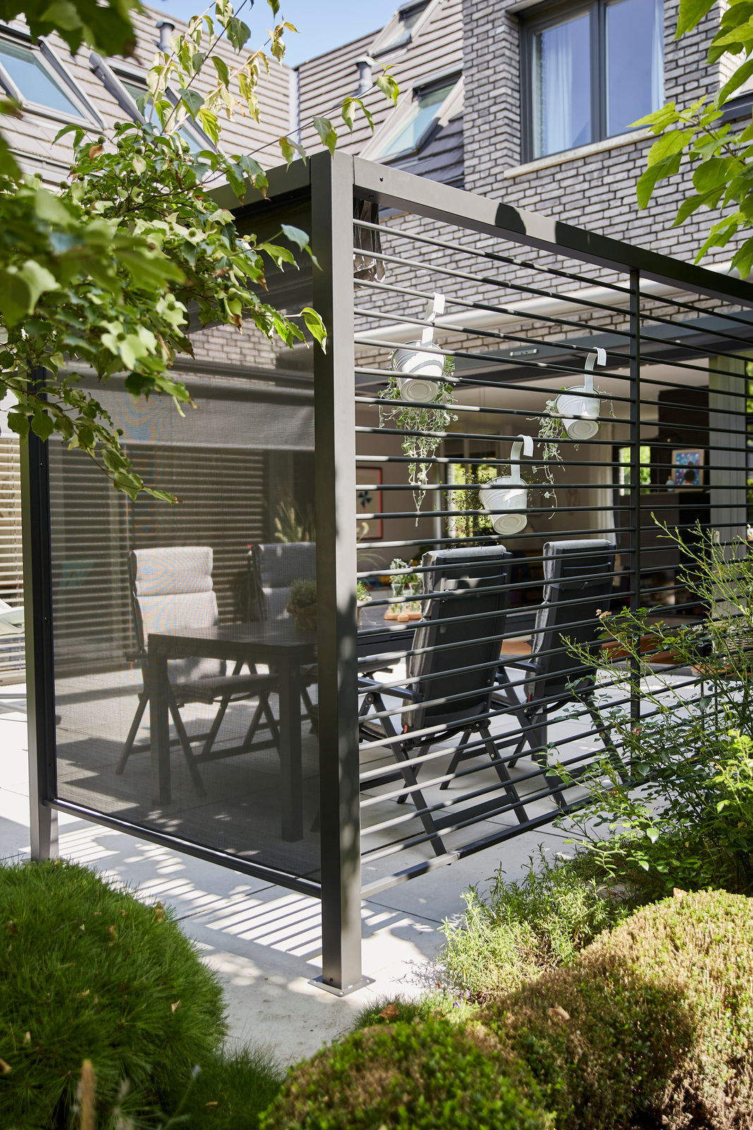 Moderner Sichtschutz aus Aluminium auf einer Terrasse, seitliche Perspektive, umgeben von Pflanzen und Gartenmöbeln.