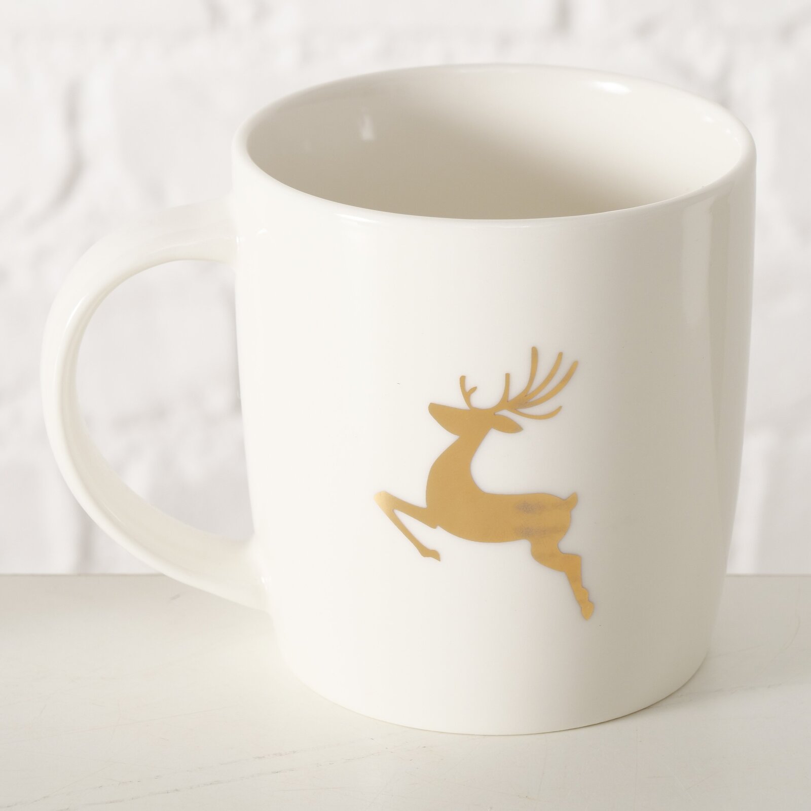 Weißer Becher mit goldfarbenem Rentiermotiv, seitliche Perspektive