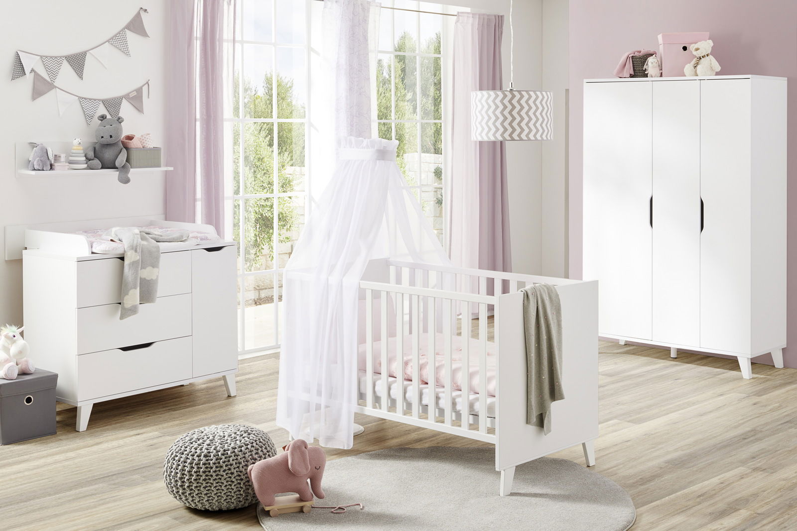 Paidi Babybett MICHA Helles und modernes Babyzimmer mit einem weißen Babybett im Vordergrund, umgeben von einem Wickeltisch und einem Kleiderschrank. Die Perspektive zeigt das Zimmer von der Seite mit Blick auf das Fenster.