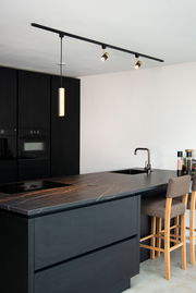 Moderne schwarze Strahler FLORIS an einer Decke montiert, beleuchten eine stilvolle Küche mit dunklen Schränken und einer eleganten Arbeitsplatte. Perspektive von der Seite.