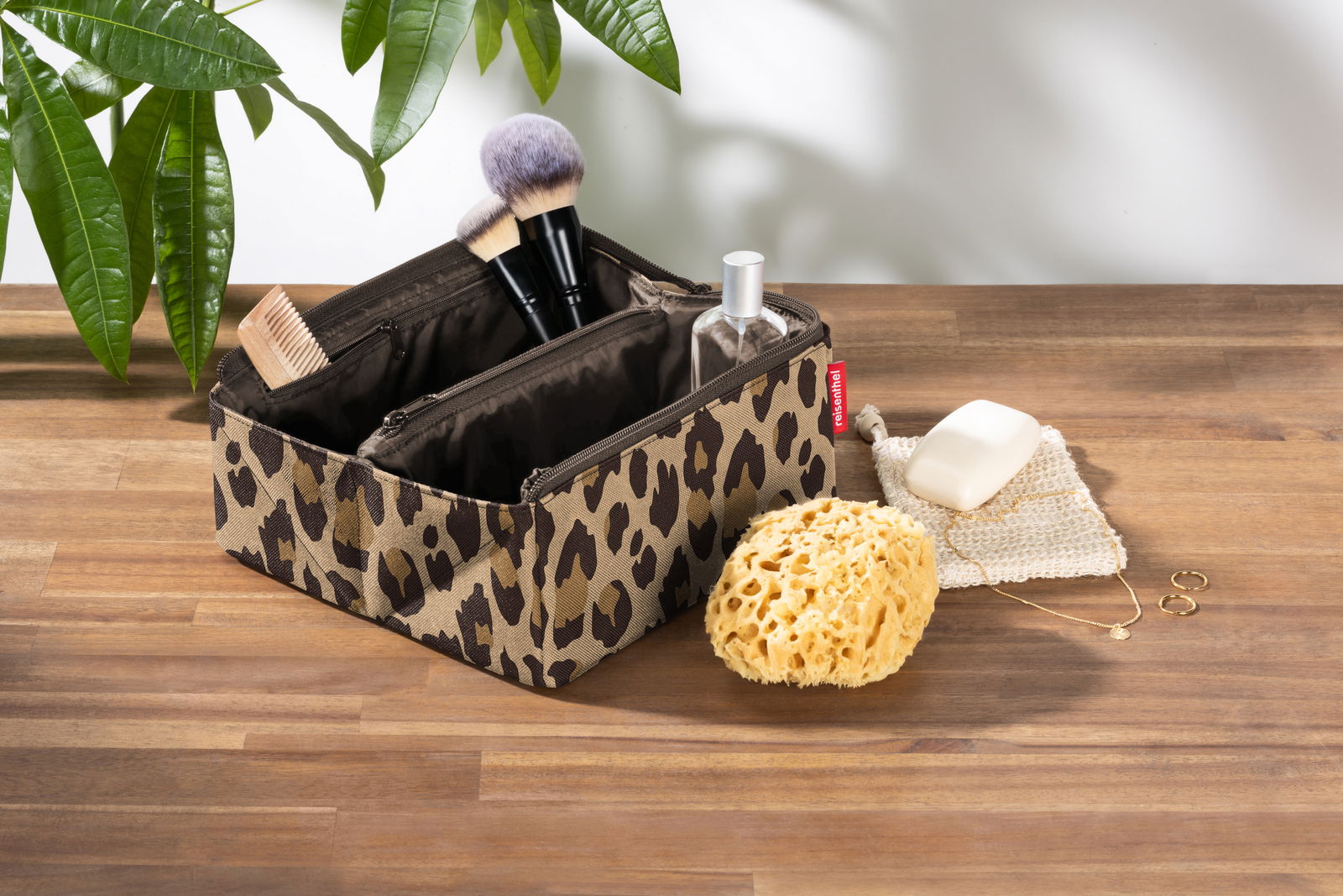 Reisenthel Fold Case LEO MACCHIATO Kosmetiktasche mit Leopardenmuster, gefüllt mit Make-up-Pinseln und Fläschchen, auf einem Holztisch von oben fotografiert.