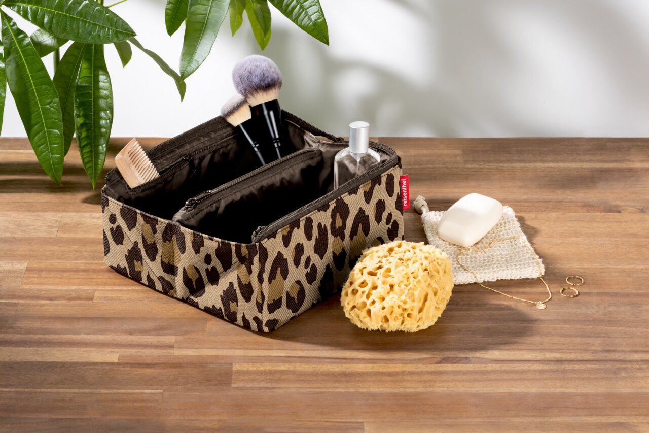 Kosmetiktasche mit Leopardenmuster, gefüllt mit Make-up-Pinseln und Fläschchen, auf einem Holztisch von oben fotografiert.