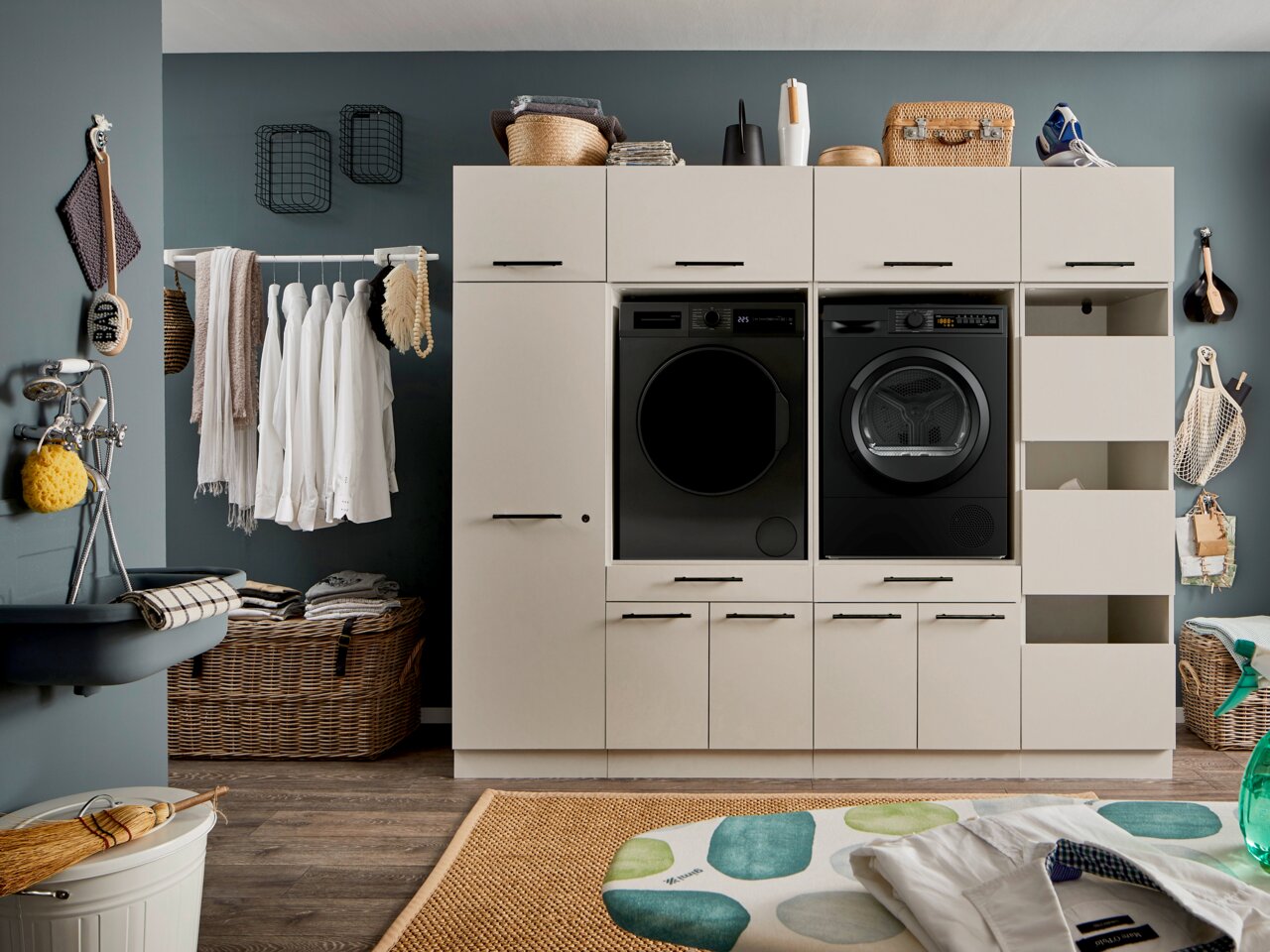 XORA Aufsatzschrank schmal PRIMUS Moderne Waschküche mit Einbauschrank in Beige, integrierter Waschmaschine und Trockner, Wäschekorb und Hängestange mit Hemden, Frontansicht auf Augenhöhe.