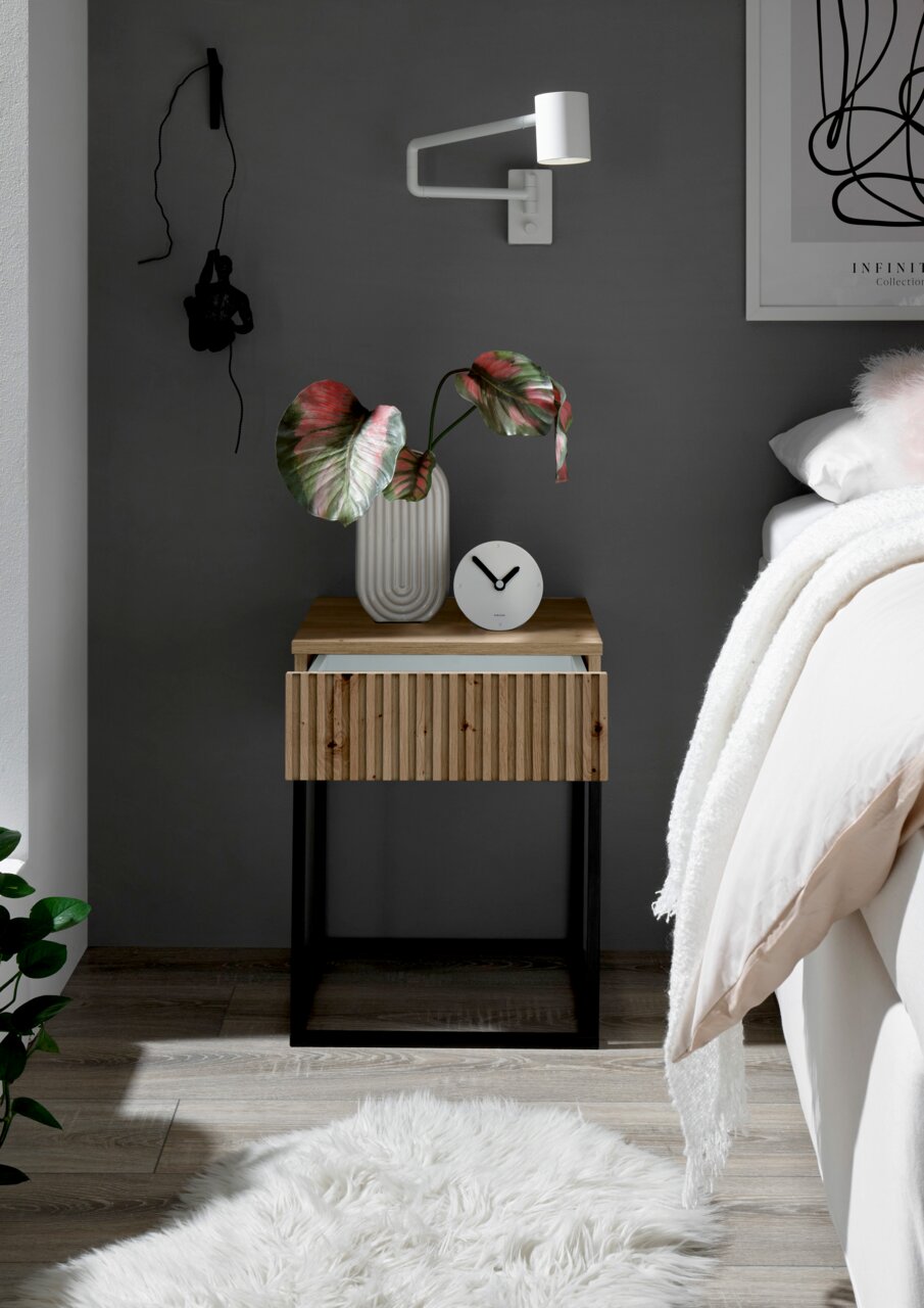 Moderne Nachtkommode mit Holzfront und schwarzem Metallgestell, dekoriert mit einer Vase und einer Uhr, aus der Perspektive eines gemütlichen Schlafzimmers.