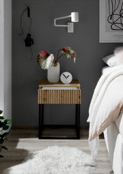 Moderne Nachtkommode mit Holzfront und schwarzem Metallgestell, dekoriert mit einer Vase und einer Uhr, aus der Perspektive eines gemütlichen Schlafzimmers.