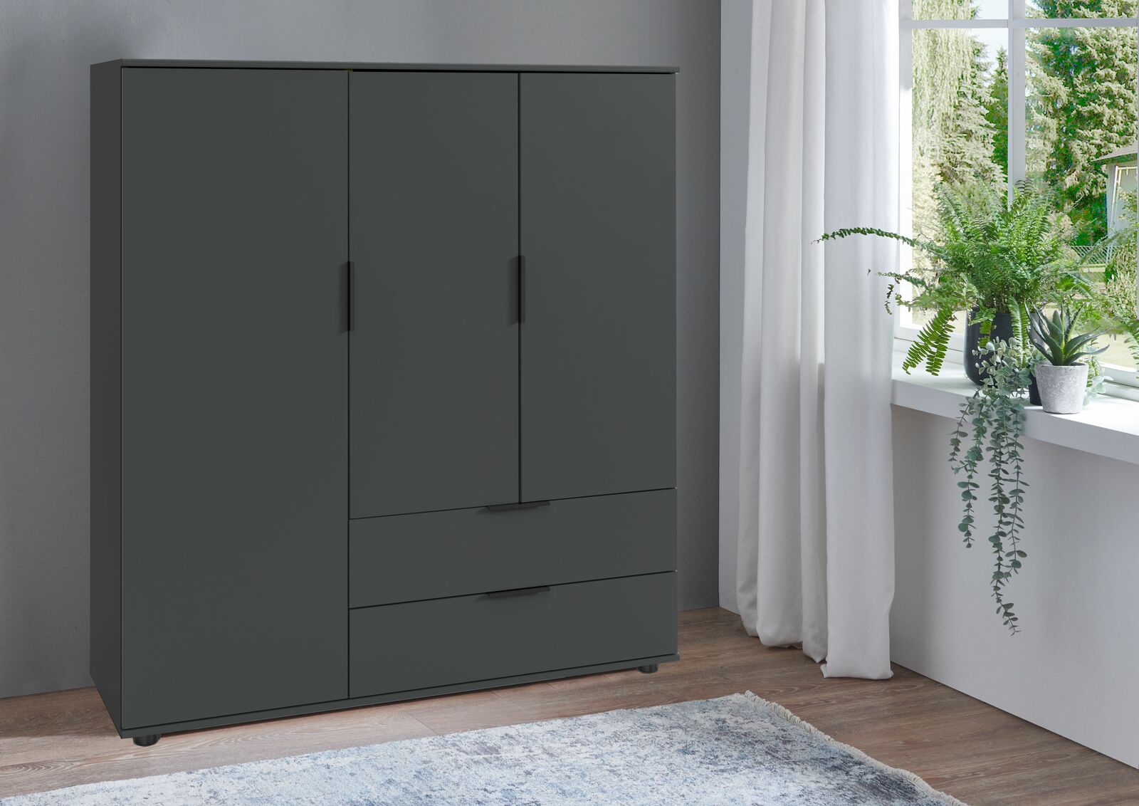 Z2 Highboard EASY PLUS Modernes, dunkelgraues Highboard mit drei Türen und zwei Schubladen, seitliche Perspektive, neben einem Fenster mit Pflanzen.