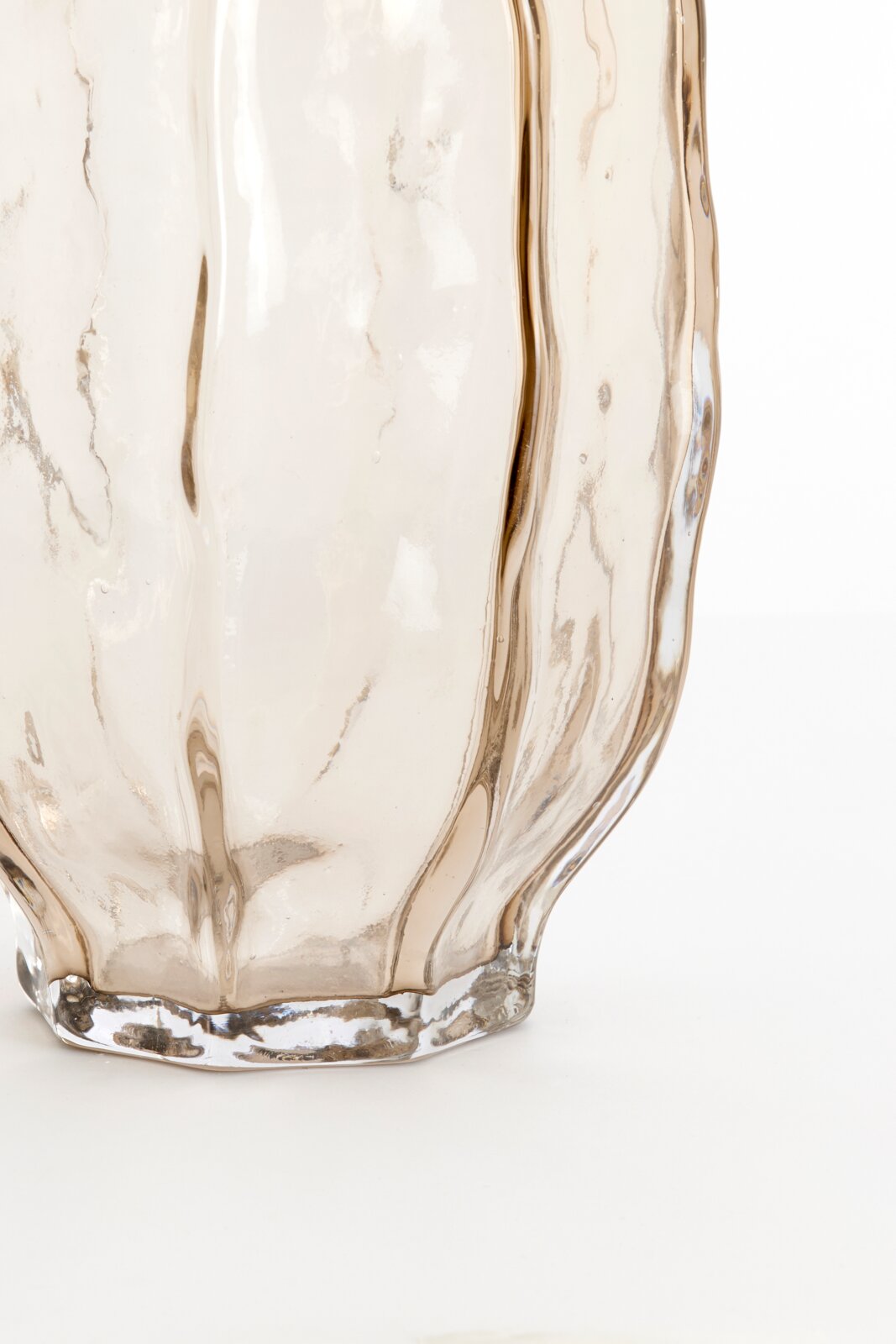 Close-up in vooraanzicht van een transparant, licht amberkleurig glazen object met organisch golvend reliëf en een dikke bodem.