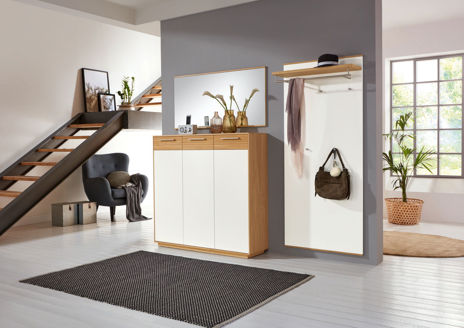 Moderne Garderobeneinrichtung mit Schuhschrank, Spiegel und Garderobenpaneel in einem stilvollen Raum mit Treppe, aus der Perspektive des Eingangsbereichs betrachtet.