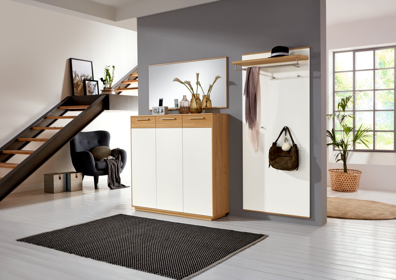 VOSS XL-Schuhkommode LOVENO Moderne Garderobeneinrichtung mit Schuhschrank, Spiegel und Garderobenpaneel in einem stilvollen Raum mit Treppe, aus der Perspektive des Eingangsbereichs betrachtet.