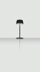 Schwarze Akku-Tischleuchte mit modernem Design, frontal abgebildet auf einer reflektierenden Oberfläche.