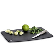 Schwarzes Schneidebrett aus Holzfaserlaminat mit Limetten, Kräutern und einem Messer, seitliche Perspektive