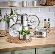 Stapel von Edelstahlkochtöpfen auf einer Küchenarbeitsplatte, mit einem Topf voller Brokkoli im Vordergrund, seitliche Perspektive.